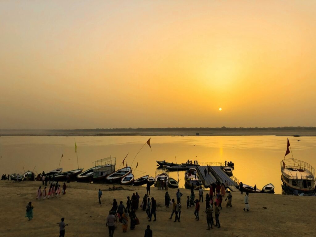 People gathered near boats at a riverbank during a golden sunset at one of the best places to visit in Varanasi, India